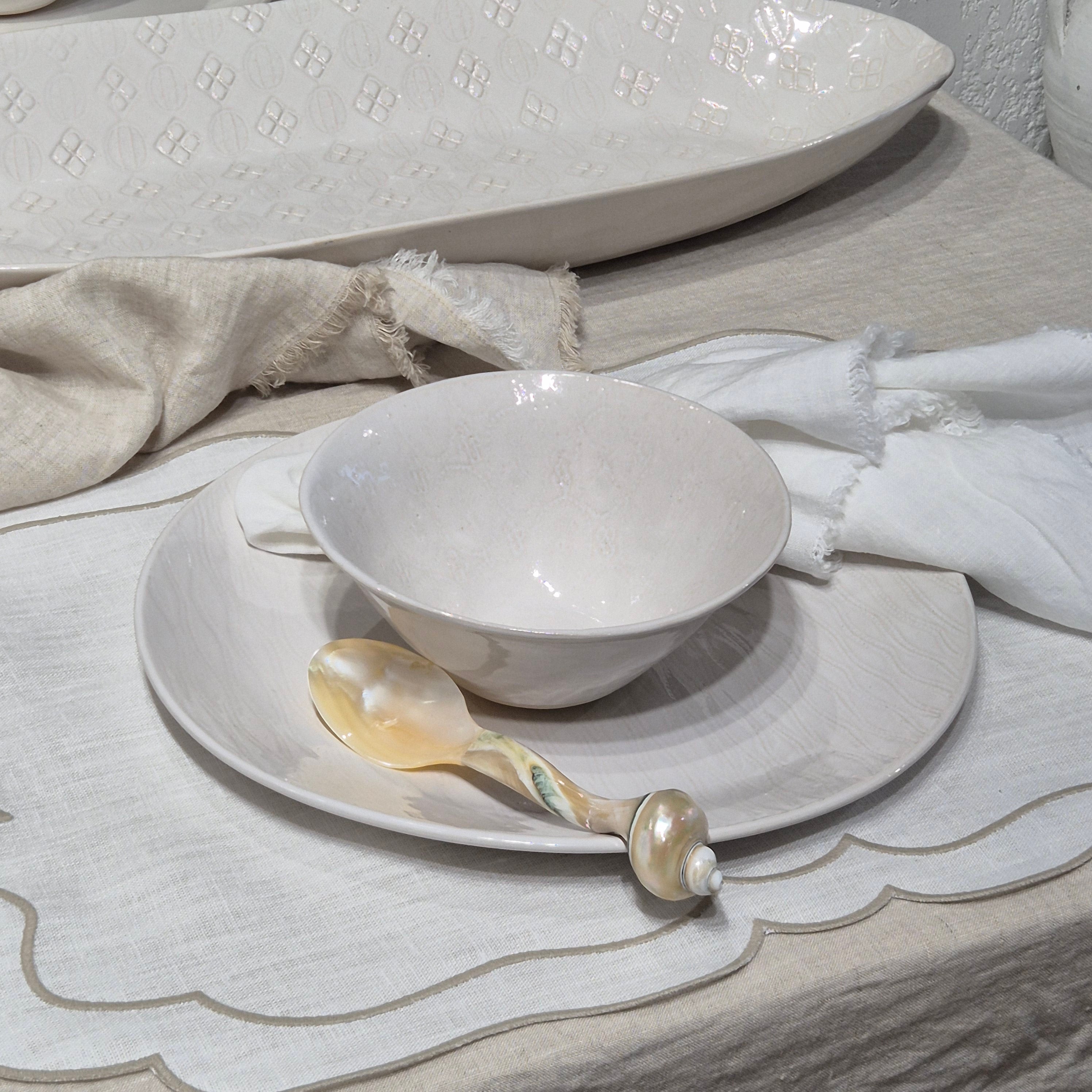 White ceramic bowl and spoon on a matching plate with a textured white cloth background