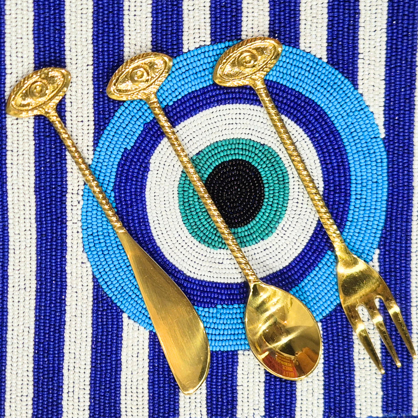 Gold spoons and fork on a blue and white striped background with a central eye design.