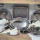 Silver platters and decorative items on a wooden surface with a wicker chair in the background.