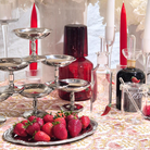 Decorative table setting with strawberries, silver platters, and red candles.