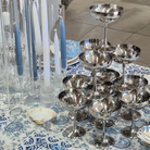 Silver cocktail glasses on a tiered stand with candles and a shell on a patterned tablecloth.